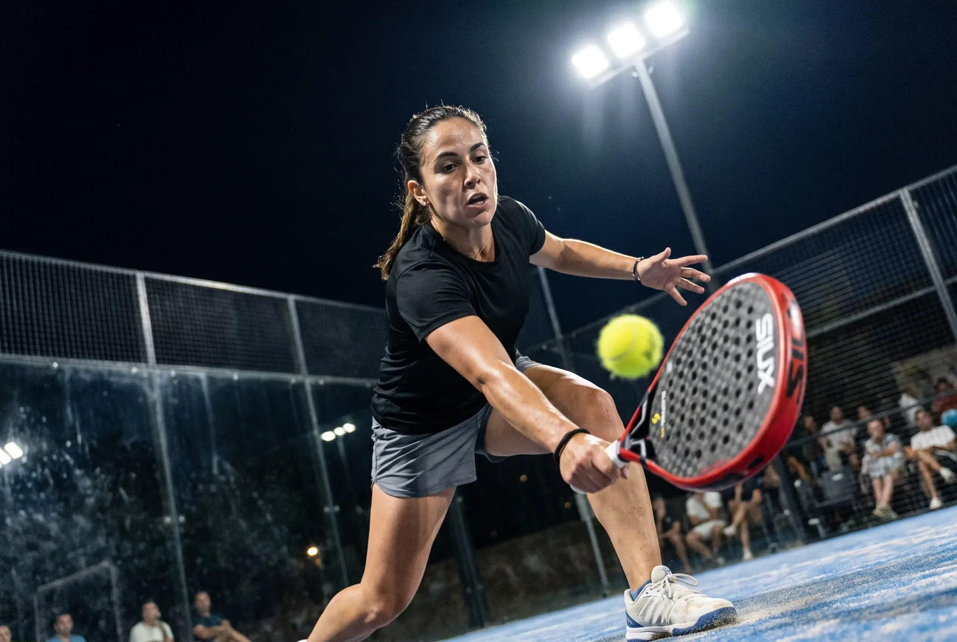 Player stretching for a low volley under floodlights with the Siux Electra Pro Fire Red